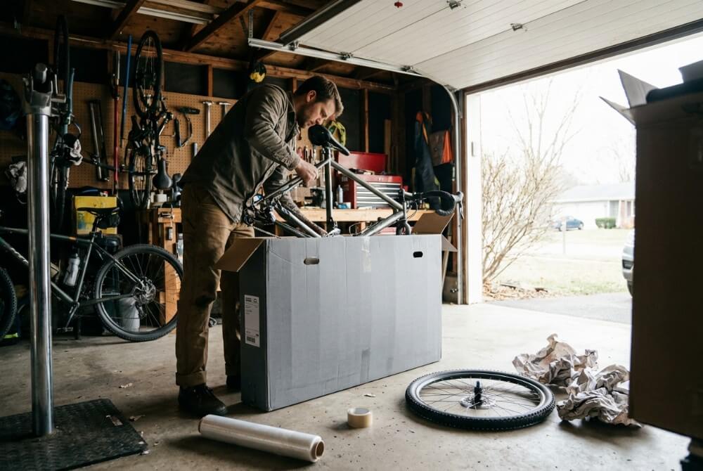 Mężczyzna pakujący zdemontowany rower do specjalistycznego kartonu w garażu, przygotowując go dla kuriera.